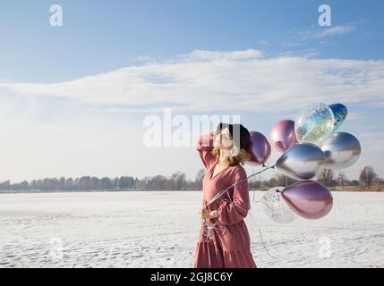 Portrait von sanften glücklich Teenager-Mädchen in rosa Kleid, schwarzer Hut, hält viele bunte Ballons in ihren Händen. Sonnigen Wintertag. Fühlt sich großartig, festlich, e Stockfoto