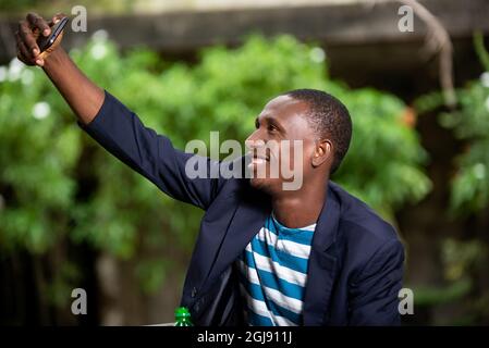 Glücklicher junger afroamerikanischer Geschäftsmann lächelt und macht Selfie-Selbstporträt mit Handy. Stockfoto