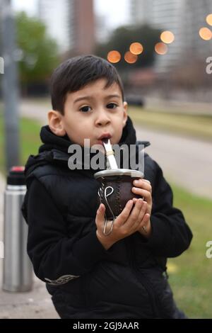 Argentinische Brünette Kind trinken Yerba Mate im Park, Blick auf die Kamera. Verschwommener Hintergrund. Im Freien, im Winter. Vertikal Stockfoto