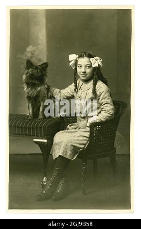 Originalfoto eines Studios aus den frühen 1900er-Jahren aus dem WW1. Jahrhundert: Ein hübsches, lächelndes britisch-asiatisches Mädchen, das lose Korkenzieherlocken mit einem Hund trägt. Großbritannien etwa 1917 Stockfoto