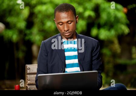 Schöner afrikanischer Geschäftsmann, der auf der Straße sitzt und am Laptop arbeitet Stockfoto