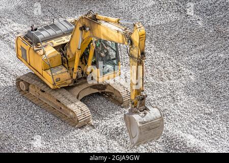 Gelber Bagger auf Schutt, der Nivelliersteine auf der Baustelle arbeitet Stockfoto