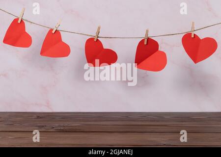 Valentinstag-Konzept. Leerer Holzdecktisch über Wandhintergrund mit herzförmiger Girlande. Stockfoto
