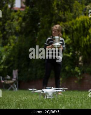 Junge Frau, die Drohne im Garten ihres Hauses fliegt. Fernbedienung mit selektivem Fokus. Stockfoto