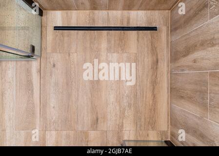 Moderner schwarzer linearer Abfluss in einem Badezimmer mit Keramikfliesen, die Holz imitieren, von oben aus gesehen. Stockfoto