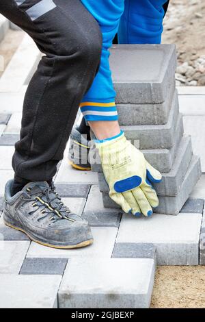 Ein Arbeiter, der Arbeitshandschuhe trägt, bringt einen Stapel Pflasterplatten zur Baustelle. Vertikales Bild. Stockfoto