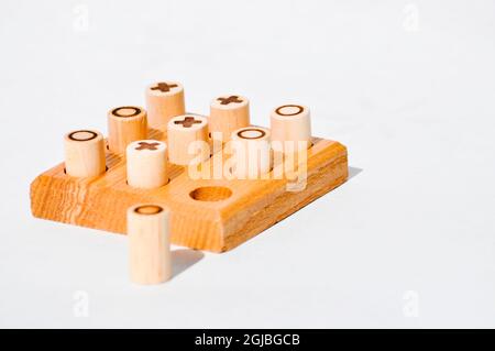 Ein handgefertigtes, hölzernes Set aus Nughts und Crosses. Die Stifte bestehen aus Holzdübel mit dem Symbol, das auf dem Brett aufgebrannt ist. Und das Brett hat 9 Löcher, die herausgebohrt wurden. Stockfoto