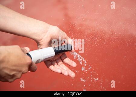 Selektiv von einem Wasserschlauch in den Händen Benetzung roten Terrassenboden Stockfoto