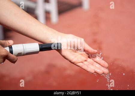 Selektiv von einem Wasserschlauch in den Händen Benetzung roten Terrassenboden Stockfoto