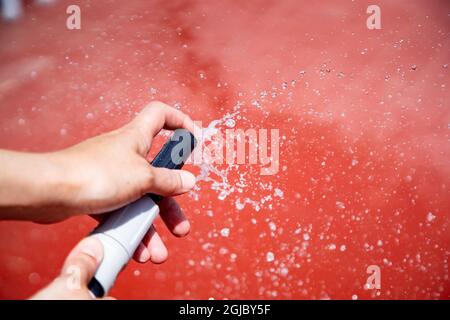 Selektiv von einem Wasserschlauch in den Händen Benetzung roten Terrassenboden Stockfoto