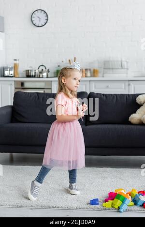 Mädchen in Spielzeug Krone und Tüllrock stehen mit Zauberstab zu Hause Stockfoto