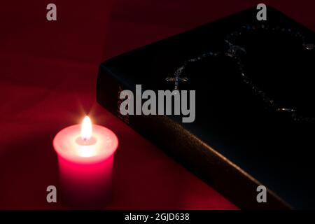 Bibel mit Kerze und Rosenkranz auf einem roten Tischtuch Stockfoto