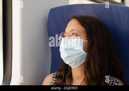 Geschäftsfrau mit Schutzmaske Blick aus dem Fenster des Zuges in Gedanken. Junge und schöne Frau mit Brille bewundern die Landschaft whi Stockfoto