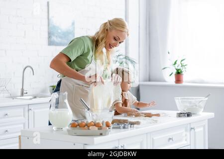 Lächelnde Frau hält selbstgemachten Teig, während sie mit ihrer Tochter in der Küche kocht Stockfoto