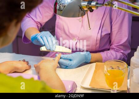 Der Meister im Schönheitssalon macht das Mädchen zu einer Maniküre. Der Master feilen die Nägel mit einer Feile an der Hand. Stockfoto