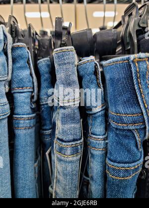 Nahaufnahme einer Reihe Jeans in Denim-Blau, die auf Kunststoffhangars im Geschäft hängen Stockfoto