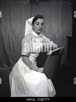 1955, historisch, eine Krankenschwester in ihrer Uniform aus dieser Zeit, die für ihr Foto posiert und ein kleines Buch in der Hand hält, England, Großbritannien. Stockfoto