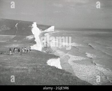 Eine Gruppe von Erwachsenen, die in den 1950er Jahren auf den Kreidekegeln der South Downs in Beachy Head, in der Nähe von Eastbourne, East Sussex, Englad, Großbritannien, spazieren. Stockfoto