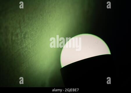 LED-Lampe. Raumbeleuchtung. Emission von Licht im Dunkeln. Ein einfaches Hintergrundlicht fällt auf die Wand. Stockfoto