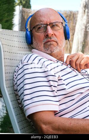 Nahaufnahme eines älteren Mannes im Ruhestand, der mit blauen Kopfhörern auf einem Rasenstuhl zur Seite schaut Stockfoto
