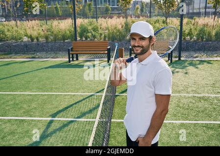 Professioneller Tennisspieler mit Schläger, der in der Nähe des Netzes auf dem Rasen-Tennisplatz posiert Stockfoto