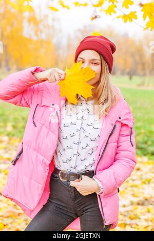 Glückliche junge Frau spielt mit fallenden gelben Blättern im schönen Herbstpark auf Naturwanderungen im Freien. Teenager-Mädchen hält Herbst orange Ahornblatt. Stockfoto