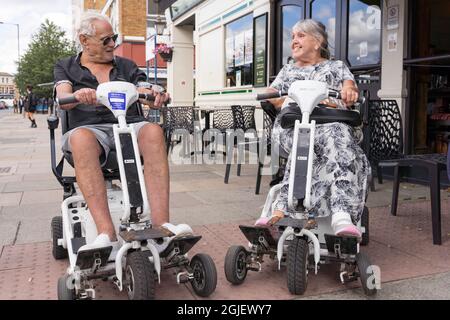 Glückliches Paar genießen Sie Roller QuinGo Fahrten an sonnigen Tag außerhalb Wetherspoons Pub Stockfoto