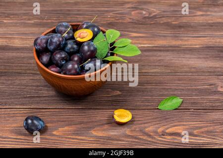 Frische reife Pflaumenfrüchte ganz und mit Blättern in einer Schüssel auf einem braunen Holztisch gehackt. Sommerernte. Stockfoto