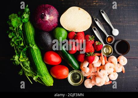 Erdbeer-Garnelen Ceviche Cocktail Zutaten auf einem Holztisch: Frisches Obst und Gemüse mit anderen Garnelen-Cocktail-Zutaten auf einem dunklen Holzbac Stockfoto