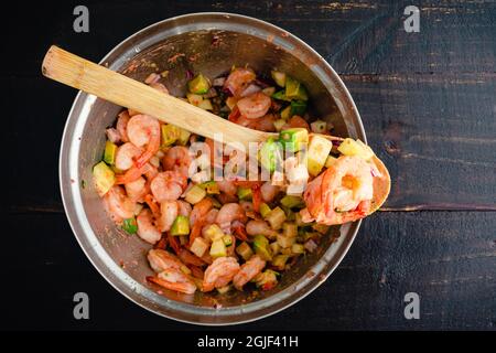 Shrimp Ceviche Cocktail Zutaten in einer Rührschüssel: Garnelen, Avocado und andere Zutaten, die mit Vinaigrette-Dressing gemischt werden Stockfoto