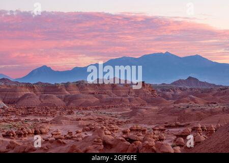 USA, Utah, Goblin Valley State Park, Sonnenuntergang Himmel über ungewöhnlichen, erodierten Hoodoo-Formationen aus Entrada-Sandstein und entfernten Henry Mountains. Stockfoto