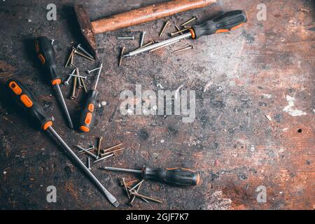 Schraubendreher, Schrauben und Hammer auf eine Holzwerkbank. Draufsicht auf Arbeitswerkzeuge mit Platz für Text. Bauwerkzeuge auf Arbeitstisch aus Holz. Backgro Stockfoto