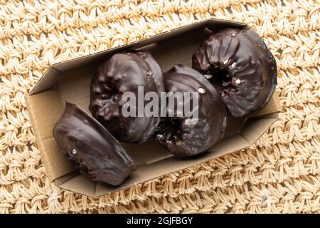 Mehrere leckere Schokoladen-Sumpflaibchen in einer Papierkiste, Nahaufnahme, auf einer Strohmatte, Draufsicht. Stockfoto