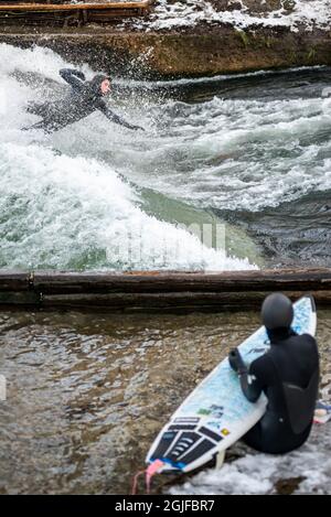 Surfer fahren stromaufwärts im Eisbach in München. Stockfoto