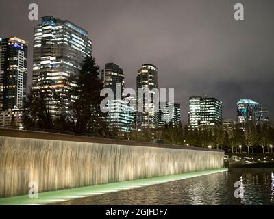 Usa, Staat Washington, Bellevue. Gläserne Büro- und Wohntürme, die nachts hinter einem Wasserfallbrunnen im Downtown Park beleuchtet werden Stockfoto