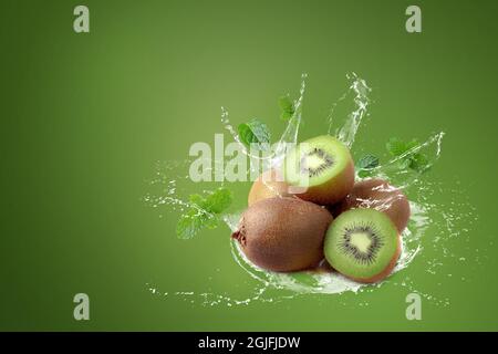 Wasser spritzt auf Kiwi-Obst und halbe Kiwi-Früchte auf grünem Hintergrund. Stockfoto