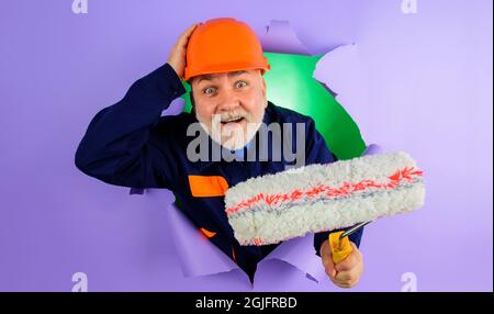 Professioneller Maler oder Dekorator mit Malerrolle, die durch ein Loch in Papier schaut. Reparatur- und Gebäudekonzept. Stockfoto