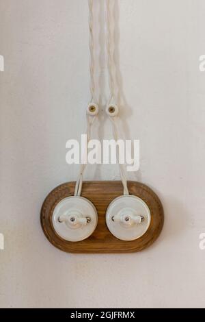 An einer leeren, verputzten weißen Wand ist ein altmodisches Schalterkabel angebracht. Elektrischer Schalter mit zwei Vintage-Schaltern. Das Thema Energie und Elektrizität Stockfoto