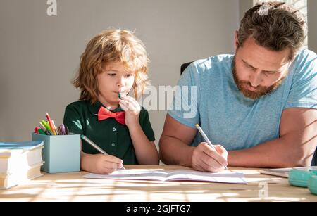 Bärtiger Vater schreibt Schulaufgaben mit seinem Jungen Sohn im Klassenzimmer, in der Schule Stockfoto