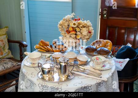 Eine formelle Einrichtung aus Desserts, silbernen Kaffee- und Teestäulen, porzellanbechern und Blumen auf einem Tisch für eine formelle Teeparty oder Feier. Stockfoto
