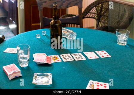 Eine halbe leere Flasche Bier schwelt nach einem Spiel auf einem Vintage-Kartentisch mit Gläsern Eis, einem Aschenbecher und einem Kartenstapel. Stockfoto