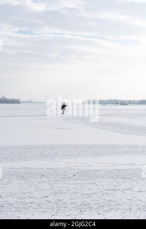 Einsamer Fischer auf Eis. Ein eineinesiger Fischer in der Mitte eines großen Sees. Angeln im Winter. Stockfoto