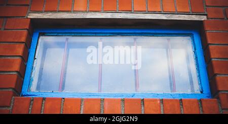 Niedrige Fenster mit altem blauen Rahmen und Eisengitter in einem orangefarbenen Ziegelgebäude. Stockfoto