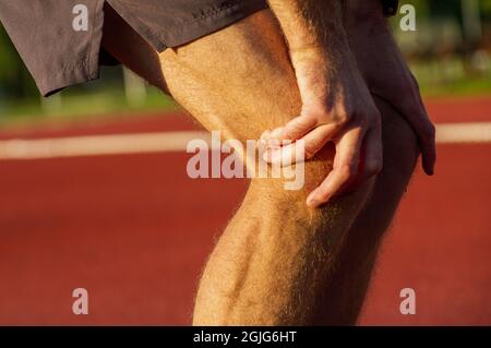 Nahaufnahme junger Laufsportler, der sich zum Laufen bereit macht, indem er Aufwärm- und Dehnungsübungen für die Beinmuskulatur macht, bevor er draußen zum Marathon auf dem Sportplatz zur Sonnenaufgangszeit trainiert Stockfoto