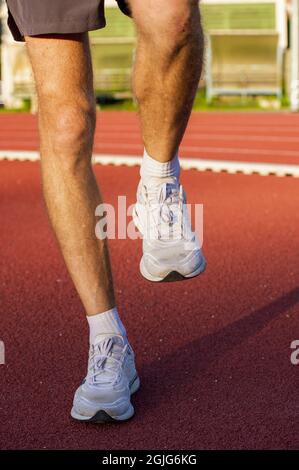 Nahaufnahme junger Laufsportler, der sich zum Laufen bereit macht, indem er Aufwärm- und Dehnungsübungen für die Beinmuskulatur macht, bevor er draußen zum Marathon auf dem Sportplatz zur Sonnenaufgangszeit trainiert Stockfoto