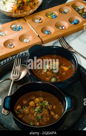 Spielen von Mancala Brettspiel beim Essen von indischem Essen einschließlich Huhn Tikka und pindi Chana Masala sowie Aloo Matar Stockfoto