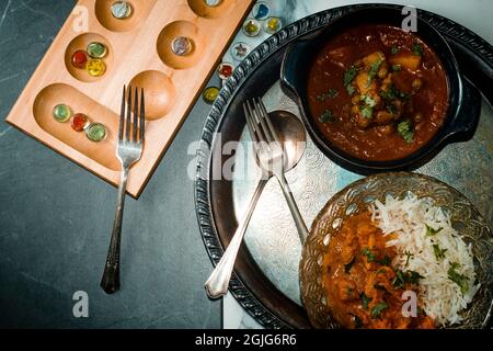 Spielen von Mancala Brettspiel beim Essen von indischem Essen einschließlich Huhn Tikka und pindi Chana Masala sowie Aloo Matar Stockfoto