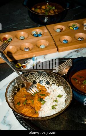 Spielen von Mancala Brettspiel beim Essen von indischem Essen einschließlich Huhn Tikka und pindi Chana Masala sowie Aloo Matar Stockfoto