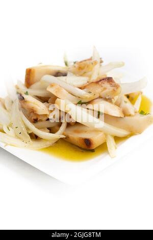 'Chocos aliñado', ein typisch spanisches Essen, Tintenfisch in Streifen mit Zwiebeln. Platte isoliert auf weißem Hintergrund. Stockfoto