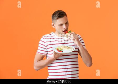 Junger Mann, der leckere Quesadilla auf farbigem Hintergrund isst Stockfoto